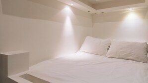 Un dormitorio minimalista con cama, paredes blancas e iluminación empotrada en el techo.