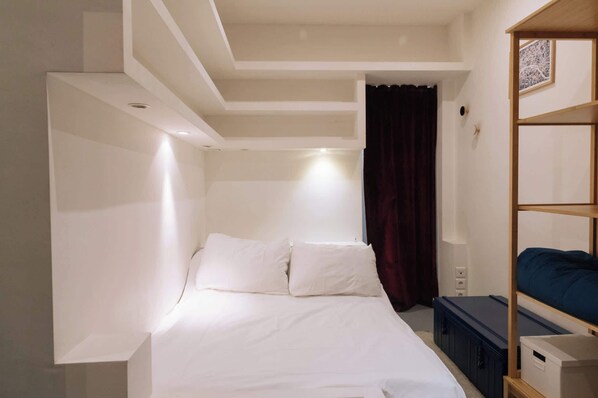 A bedroom with a bed, a wooden shelf, and a dark curtain.
