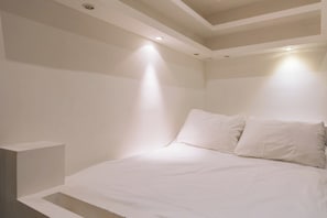 A minimalist bedroom with a bed, white walls, and recessed ceiling lighting.