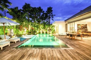 A wooden deck with a swimming pool, lounge chairs, and a dining area with a table and chairs. - Mette 3br Villa (Canggu)