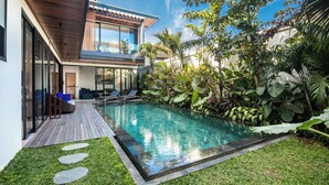 Une maison moderne dotée d’une piscine, d’une terrasse en bois et d’une végétation luxuriante.