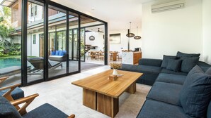 Un salon moderne avec une table basse en bois, des canapés foncés et une porte en verre donnant sur un balcon.