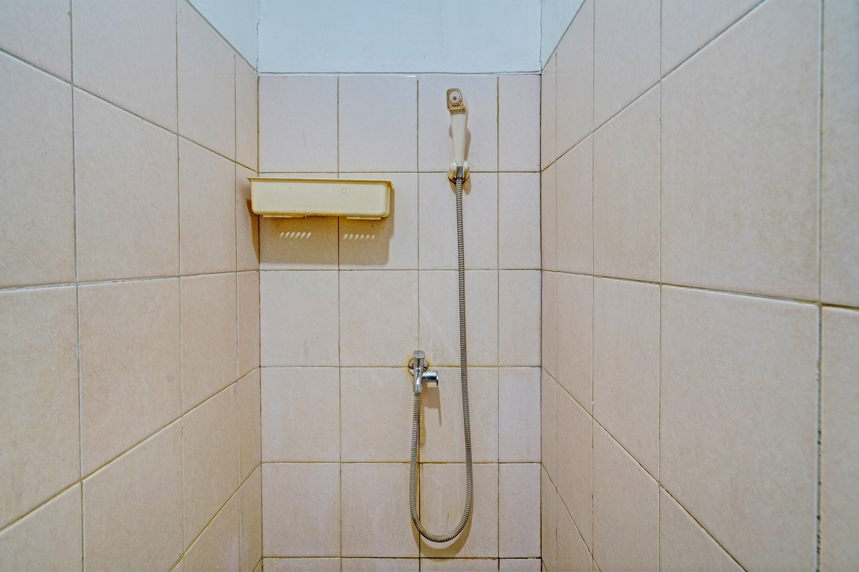 A shower area with a handheld showerhead and a wall-mounted control panel.
