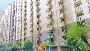 Een hoog appartementencomplex met meerdere balkons en een speelruimte met glijbanen en schommels.