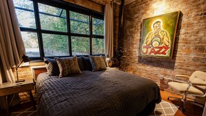 Une chambre avec un grand lit, un bureau, une chaise et une grande fenêtre.