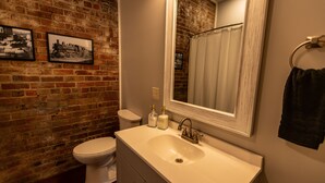 Une salle de bain avec un mur en briques, un lavabo blanc, des toilettes et un miroir.