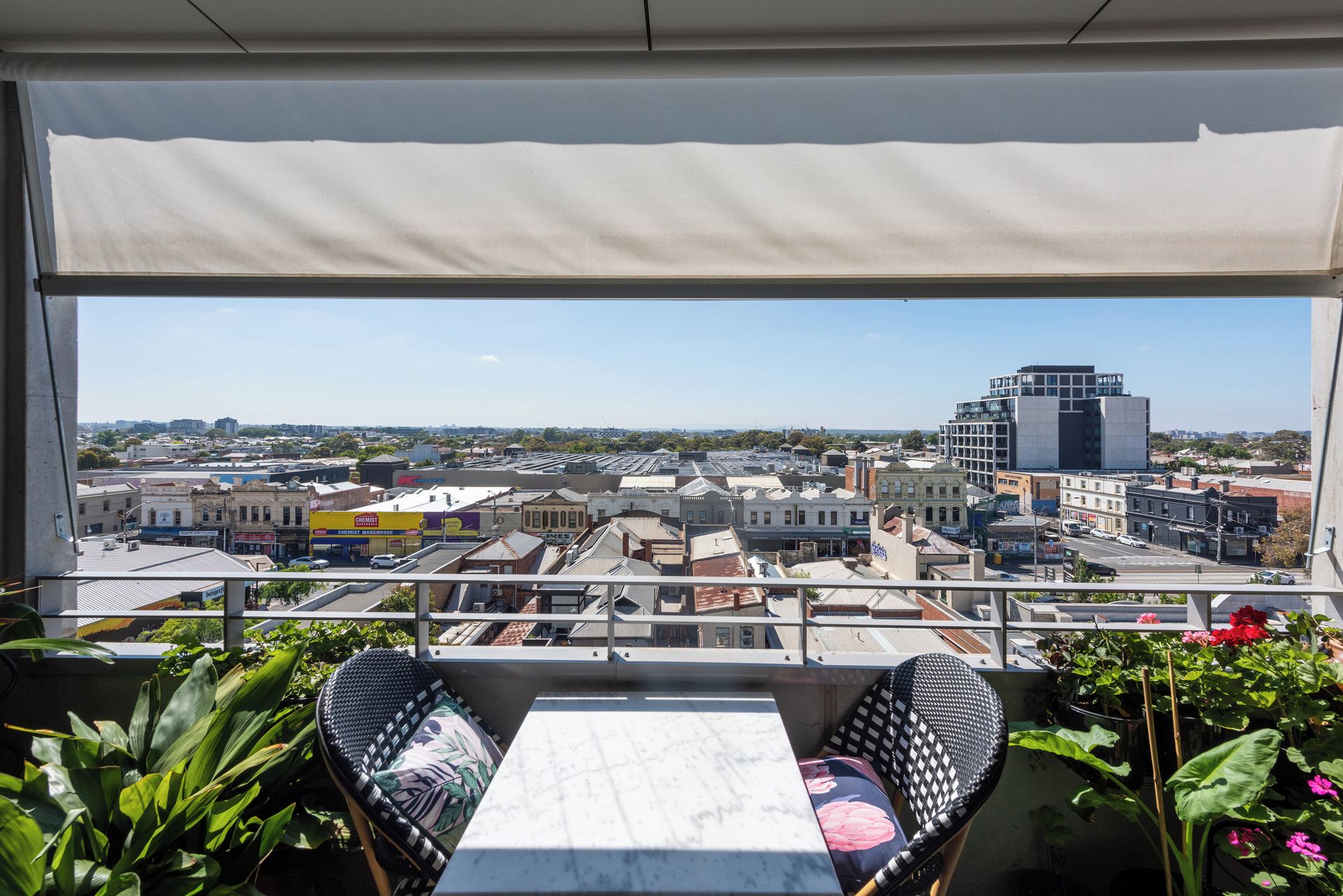 Ein Balkon mit Tisch und Stühlen, der auf einen Stadtblick mit verschiedenen Gebäuden und einem klaren Himmel blickt.