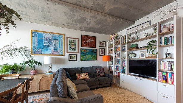 Ein Wohnzimmer mit grauem Sofa, einer Bücherwand und einem Flachbildfernseher.