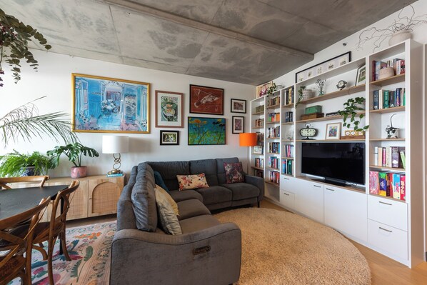 A living room with a grey sofa, a bookshelf, and a flat-screen TV.