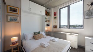 Ein Schlafzimmer mit Bett, Nachttisch, Fenster und Einbauschränken.