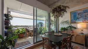 Ein Essbereich mit Tisch und Stühlen, Blick auf die Stadt durch große Fenster und verschiedene Kübelpflanzen.