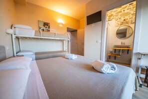 Ein Hotelzimmer mit Etagenbett, einem Einzelbett, einem Badezimmer mit Steinwand und einem kleinen Schreibtisch mit Spiegel.