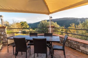 Eine Terrasse im Freien mit Tisch und Stühlen, eine Steinmauer und Blick auf eine hügelige Landschaft.