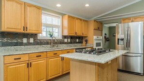 A kitchen with wooden cabinets, granite countertops, a stainless steel refrigerator, and a built-in stove.