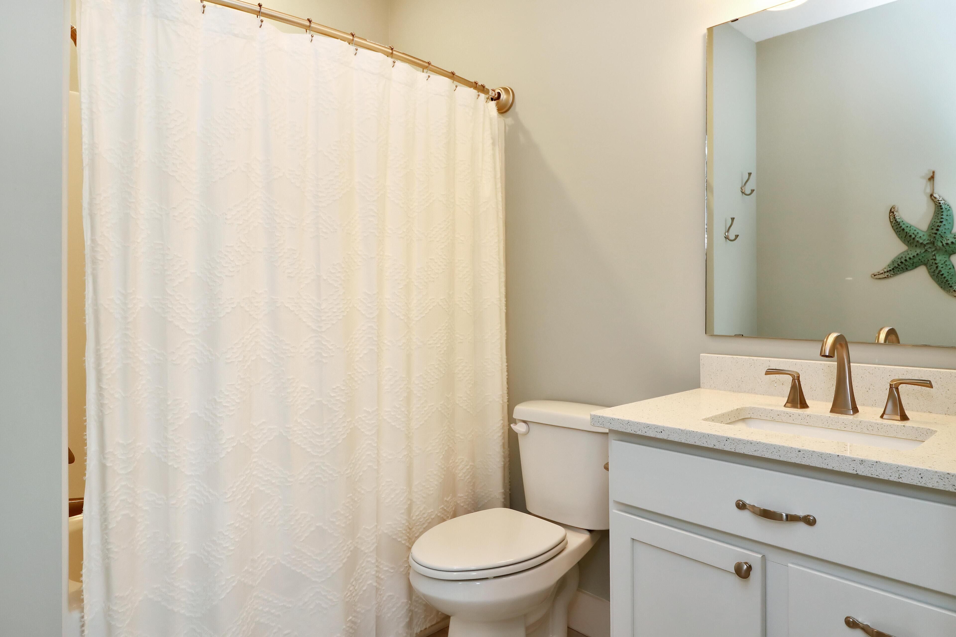 Une salle de bain avec des toilettes, un lavabo avec un miroir au-dessus et un rideau de douche.