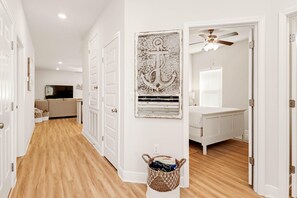 A hallway with wooden flooring, white doors, a ceiling fan, and a wall-mounted anchor decoration. - The Blue Bird (Port St. Joe)