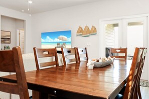 A dining area with a wooden table and chairs, a painting of a beach scene, and a sailboat decoration on the wall.