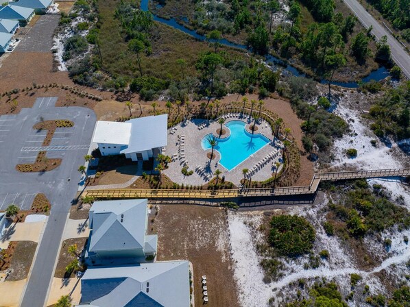 An aerial view of a resort with a central pool, a parking lot, and surrounding vegetation.