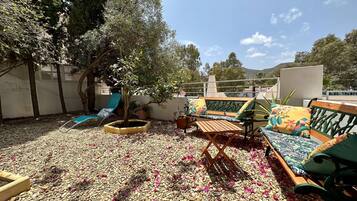 Relax on the rooftop terrace with a wooden bench and lounge chair, surrounded by pebbles and a shaded area under a small tree.