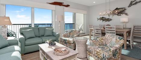 A spacious living room with a green sofa, a patterned armchair, and a dining area with a wooden table and chairs.