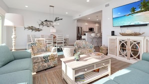 A spacious living room with a large flat-screen TV, comfortable seating, and a kitchen area in the background. - The Vue 2C (Port St. Joe)