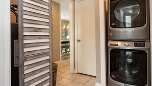 A laundry room with a stacked washer and dryer, a door leading to a dining area, and a tiled floor. - Castaway (Port St. Joe)