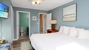 A bedroom with a bed, a ceiling fan, a TV, and a painting on the wall. - Castaway (Port St. Joe)