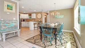 A dining area with a wooden table and blue chairs, a bench, and a chandelier. - Castaway (Port St. Joe)