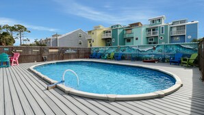 A swimming pool with a wooden deck, surrounded by colorful chairs and a mural. - Castaway (Port St. Joe)