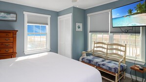 A bedroom with a bed, a wooden chair, a dresser, and a television displaying a beach scene. - Castaway (Port St. Joe)