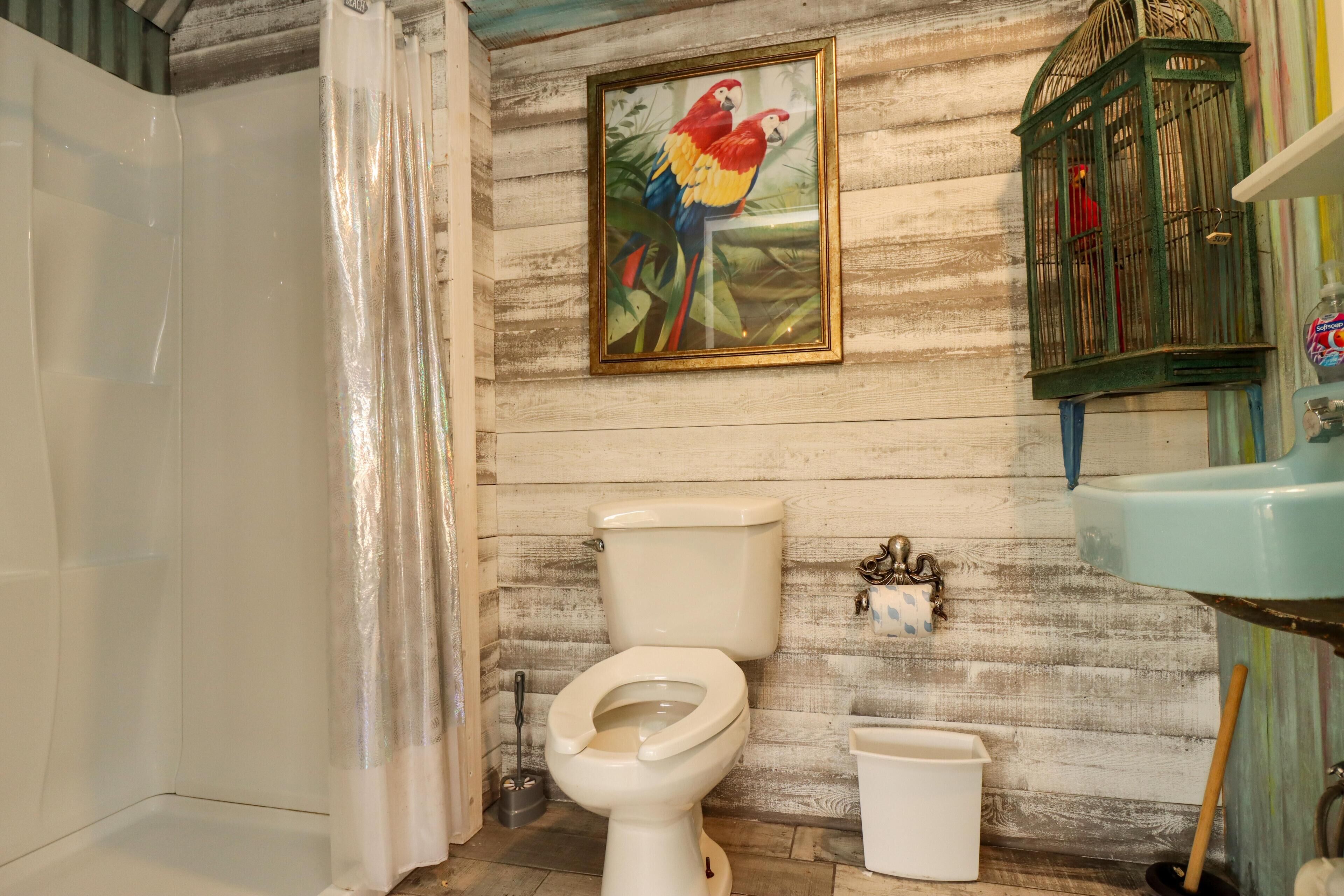 A bathroom with a wooden wall, a toilet, a sink, a birdcage, and a shower curtain.