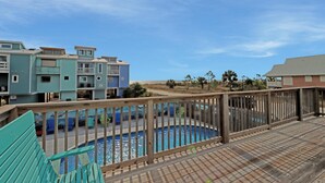 A pool area with a wooden deck, a pool, and buildings in the background. - Castaway (Port St. Joe)