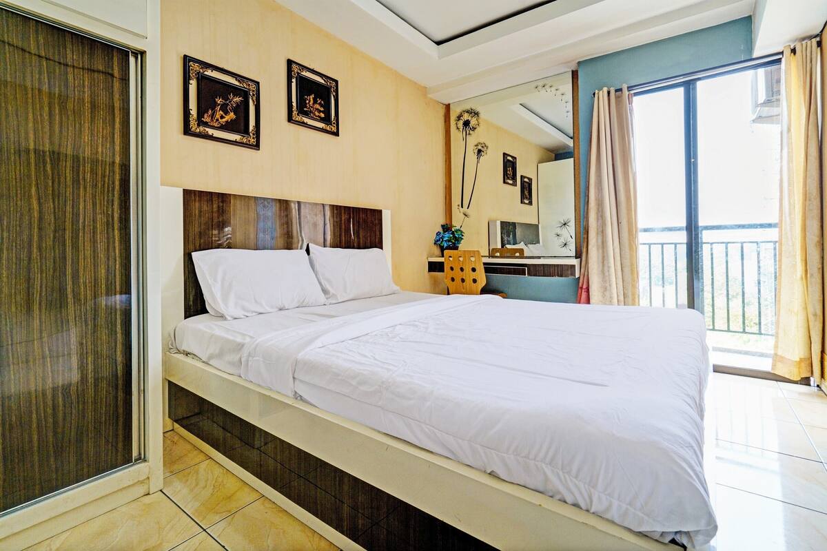 Ein Hotelzimmer mit Bett, Schreibtisch, Stuhl, einem Fenster mit Vorhängen und einer Wand mit gerahmten Bildern.