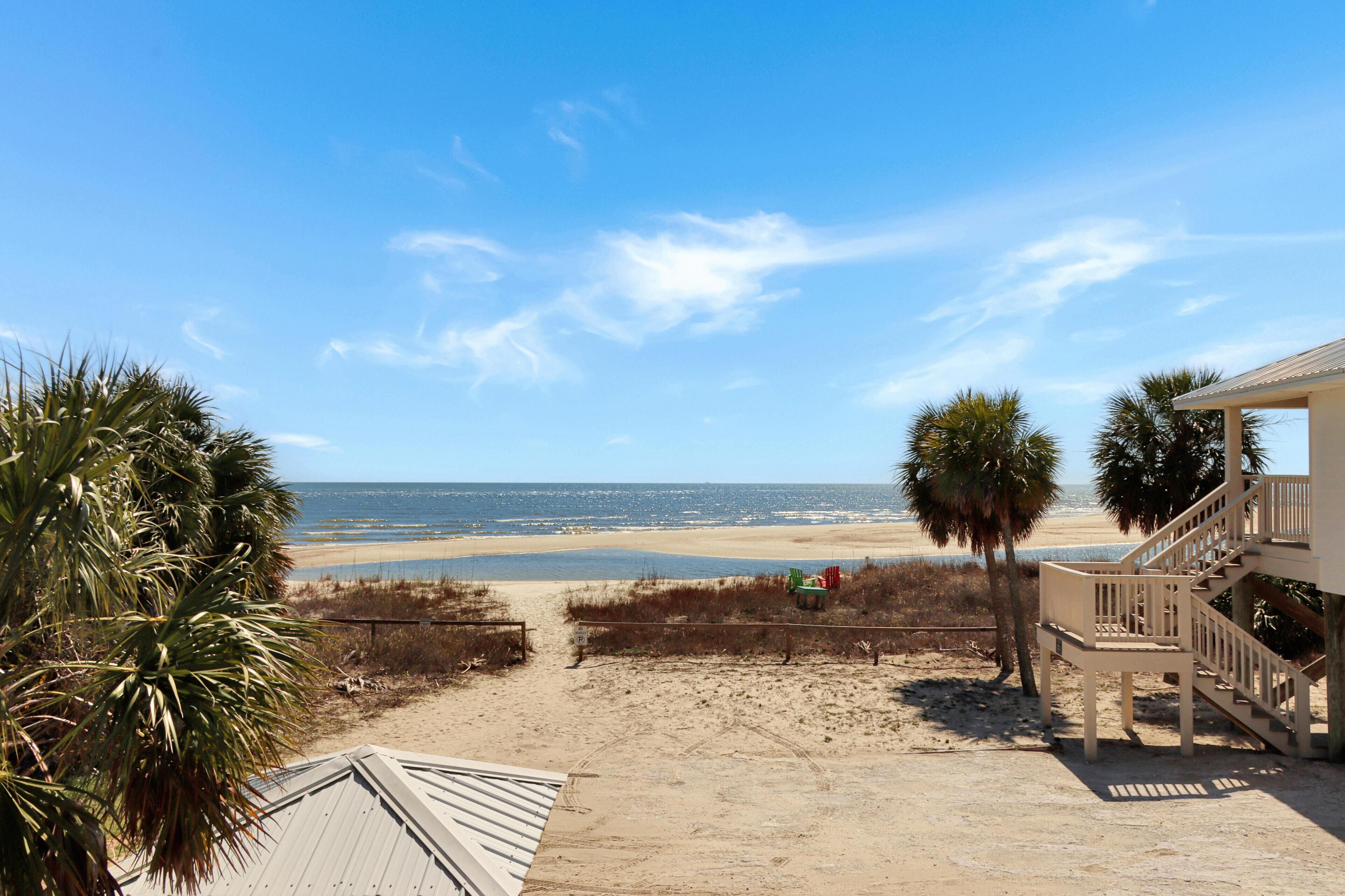 A beach view with a wooden deck, palm trees, and a staircase leading to a building.