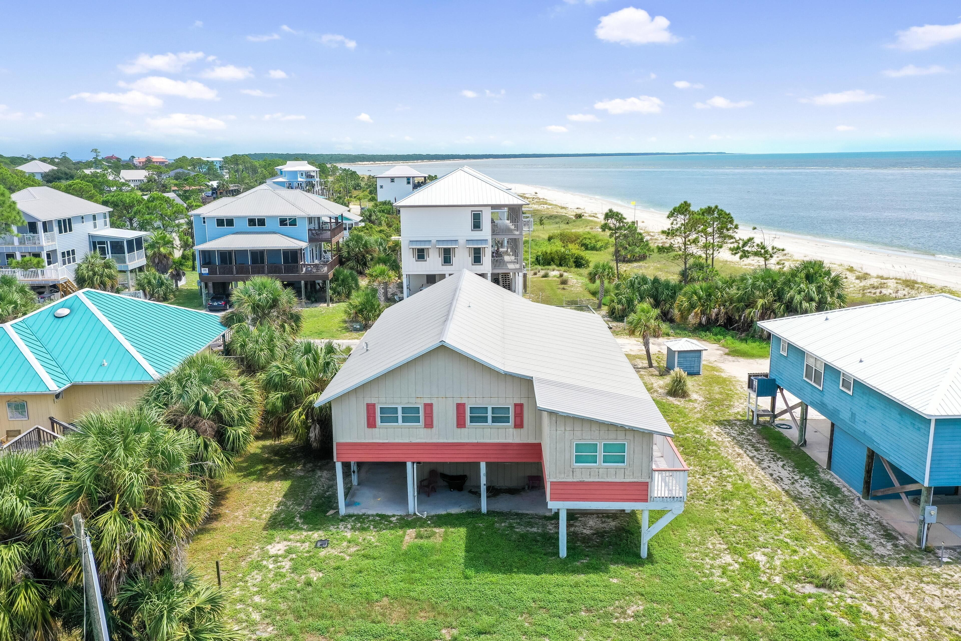 A coastal residential area with houses featuring red and blue exteriors, a beach, and a clear sky.