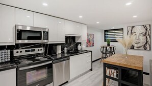 Una cocina moderna con electrodomésticos de acero inoxidable, armarios blancos y un comedor con mesa y sillas de madera.
