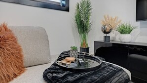 Una sala de estar moderna con un sofá gris, una mesa de centro redonda negra con objetos decorativos, una planta verde alta y un globo terráqueo en un estante.