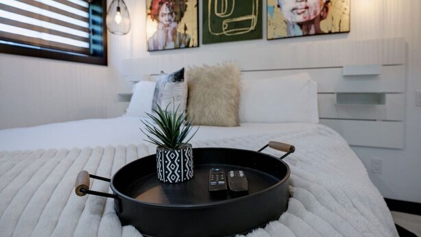 Un dormitorio moderno con cama, una bandeja con planta y controles remotos, y una obra de arte en la pared.
