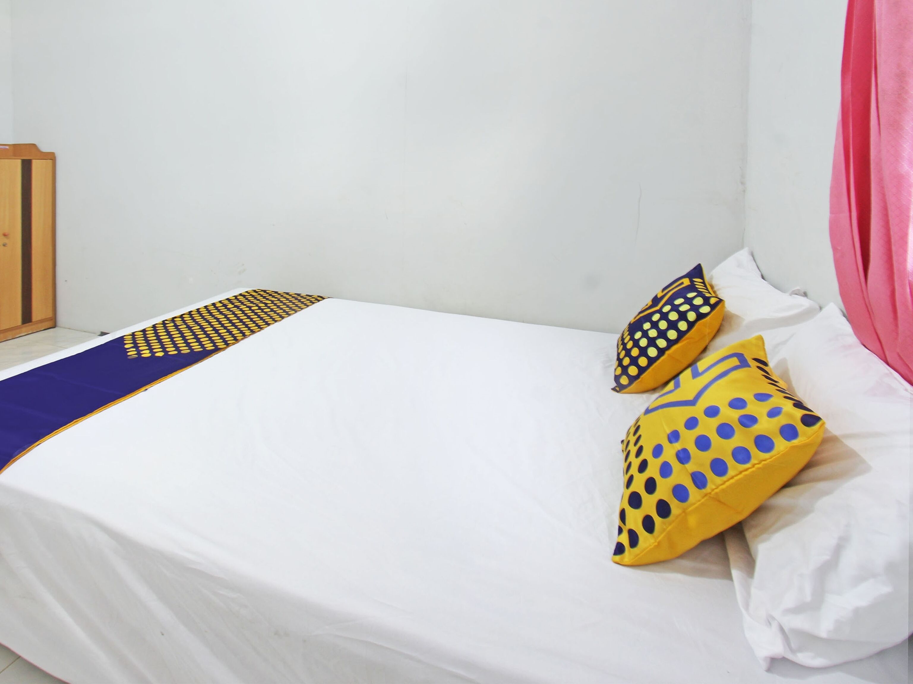 Una cama con sábana blanca, dos almohadas con lunares amarillos y azules, y un corredor azul y amarillo estampado.