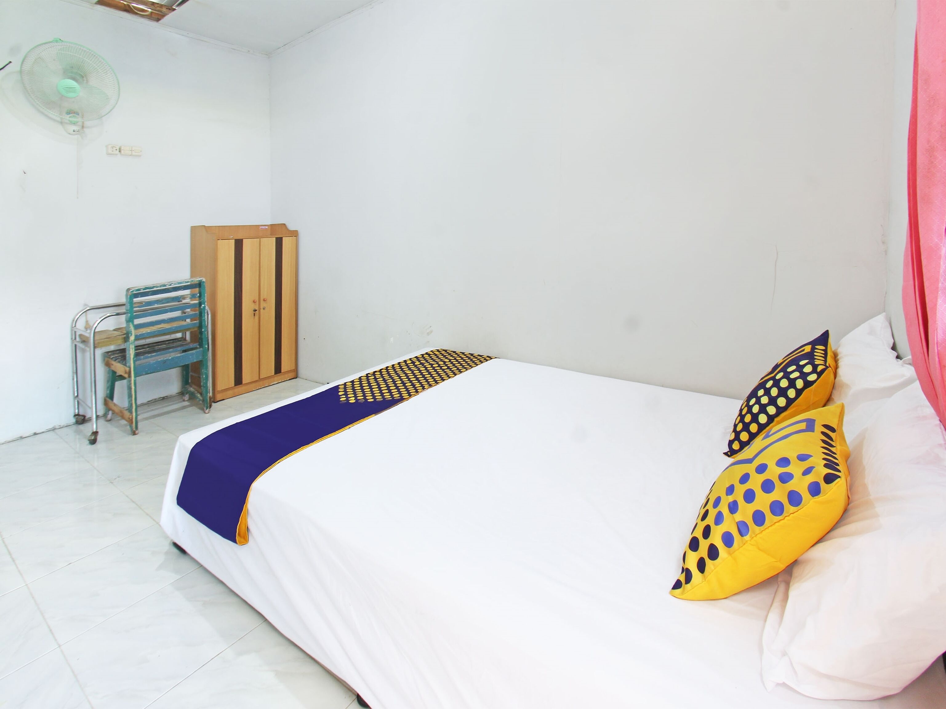 A room with a bed, a chair, a wardrobe, and a fan.