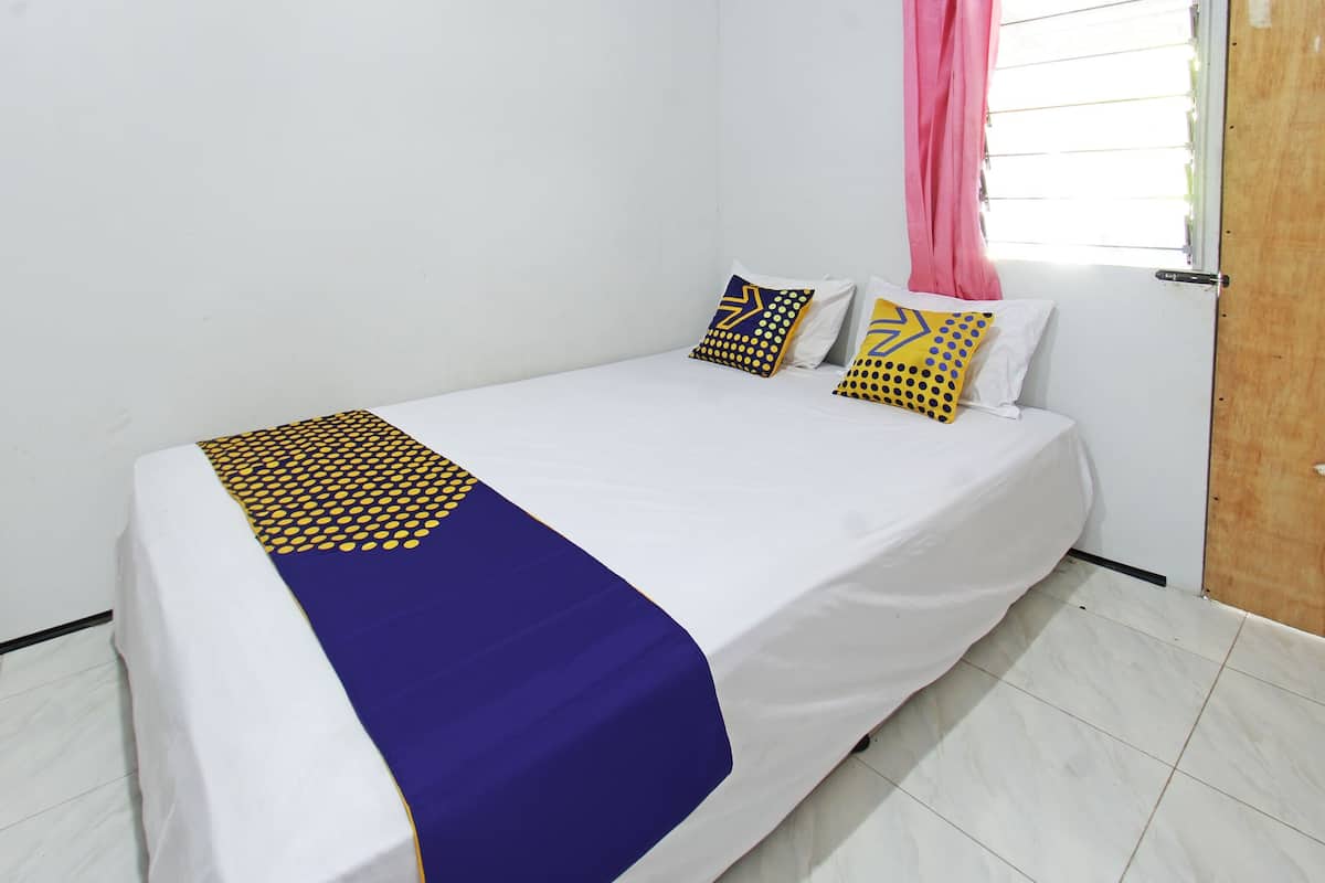 Ein Einzelbett mit weißer Matratze, einer Bettdecke in Blau-Gelb-Muster und zwei dekorativen Kissen mit geometrischen Designs.