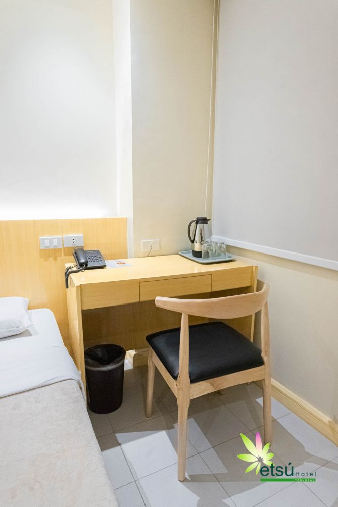A hotel room with a wooden desk, a chair, a telephone, a coffee maker, and a trash bin.