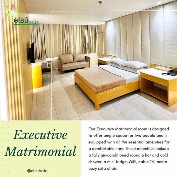 An Executive Matrimonial room with a bed, sofa, and a TV. It includes amenities like air conditioning, a mini fridge, WiFi, cable TV, and a sofa chair.