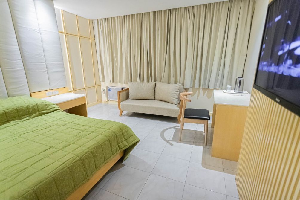 A hotel room with a bed, a sofa, a TV, and a small table with a lamp.