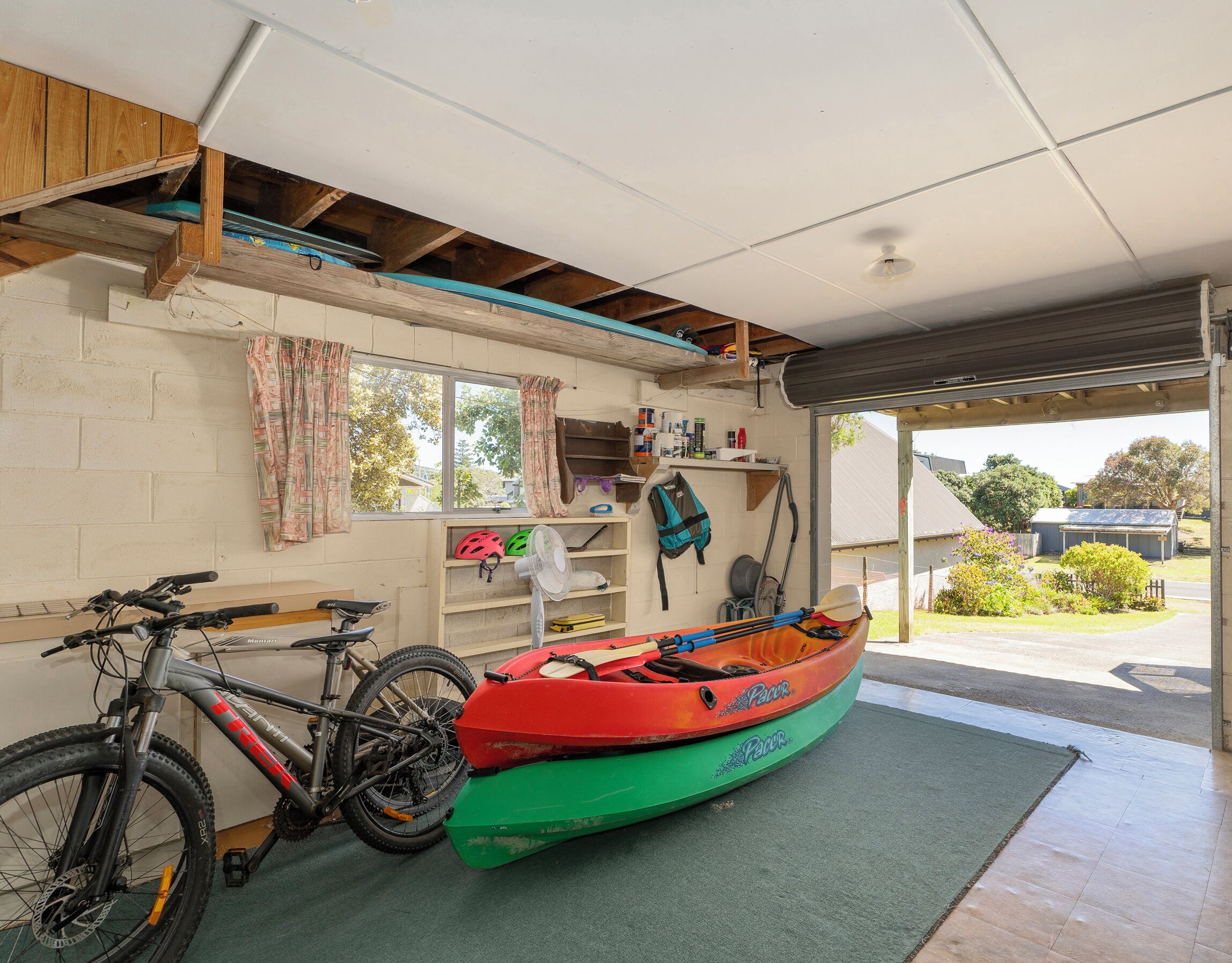 A garage with a bicycle, a kayak, and a fan.