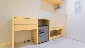 A compact room with a built-in desk, a small refrigerator, and a shelf.