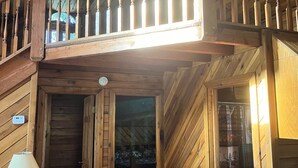 A wooden cabin interior with a loft bedroom, a sofa, a lamp, and a trash bin. - NEW RIVER GORGE CABINS-ALMOST HEAVEN (Lansing)