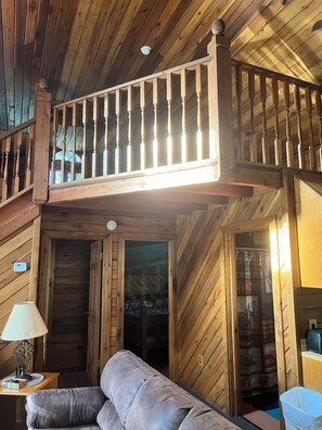 Ein Holzblockhaus-Innenraum mit Schlafzimmer im oberen Bereich, einer Couch, einer Lampe und einem Mülleimer.