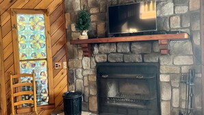 A stone fireplace with a TV above it, a wooden chair, and a small Christmas tree. - NEW RIVER GORGE CABINS-ALMOST HEAVEN (Lansing)