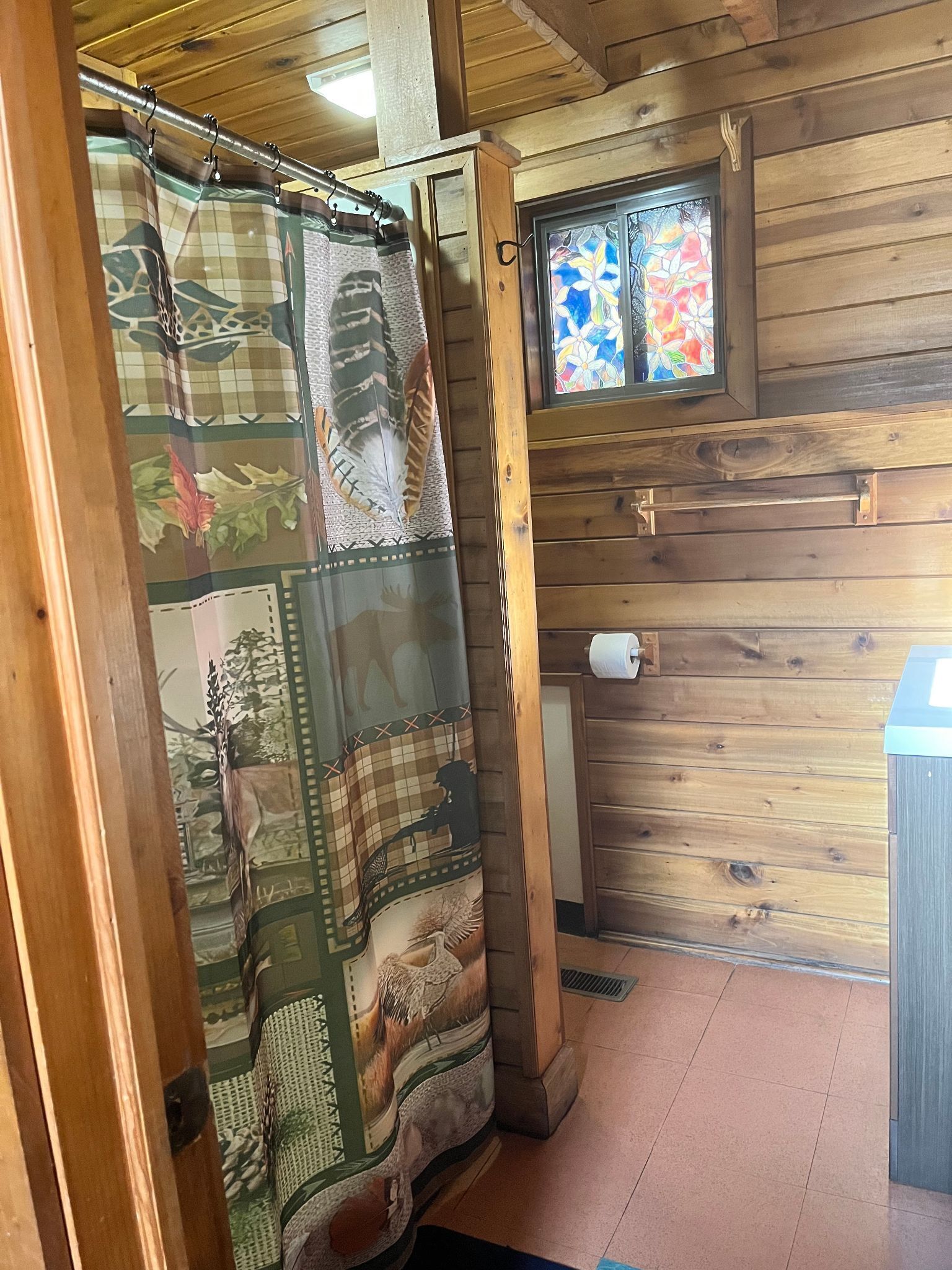 A bathroom with wooden walls, a shower curtain with animal prints, and a stained glass window.